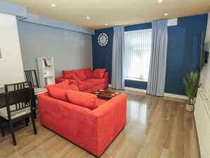 A living room with a red sofa, a wooden coffee table, a clock on the wall, and a window with curtains. - No.1 Spa Mill Lodge (Huddersfield)