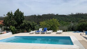 Una piscina con sillones de descanso, rodeada de árboles y un paisaje montañoso.