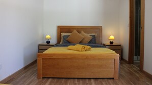 Un dormitorio con cama de madera, dos mesitas de noche con lámparas, suelo de madera y una puerta.