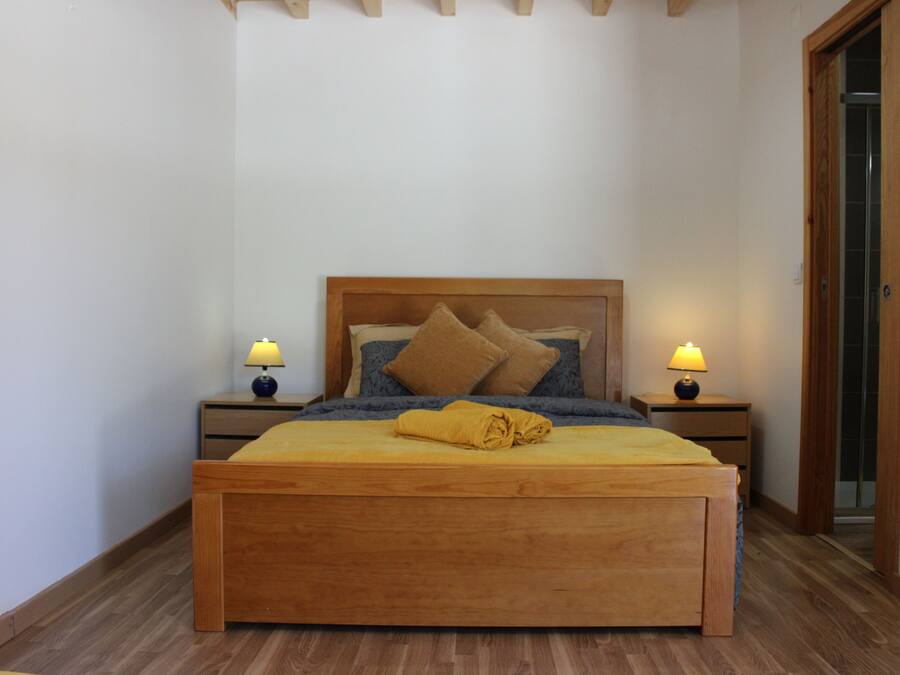 Un dormitorio con cama de madera, dos mesitas de noche con lámparas, suelo de madera y una puerta.