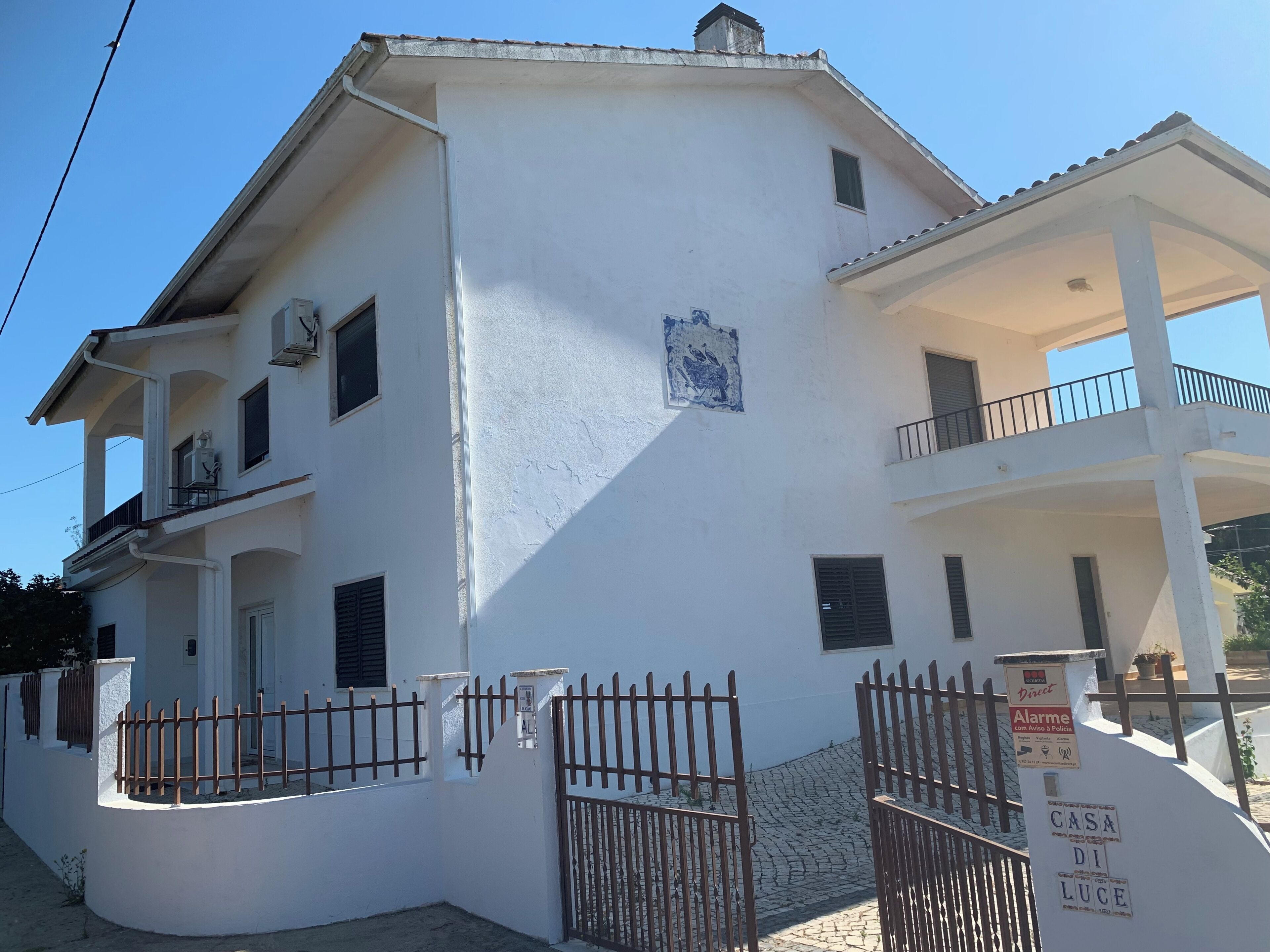 A two-story white building with a balcony, a gated entrance, and a sign indicating a police advisory.
