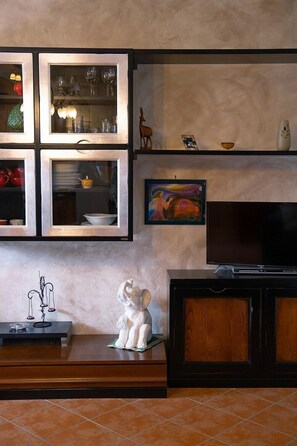 A living room with a TV, a fireplace, and a shelf with decorative items. - Via della Musica - One Bedroom House, Sleeps 3 (Vicchio)