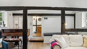 Une pièce avec un banc en bois, un canapé, un piano et une vue sur une cuisine, visible à travers une porte ouverte.