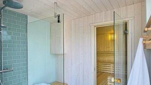 Une salle de bain moderne avec un plafond en bois, une douche en verre, un banc et un sauna visible à travers une porte en verre.