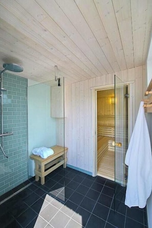 Ein modernes Badezimmer mit Holzboden, einer Duschkabine aus Glas, einer Sitzbank und einer Sauna, die durch eine Glastür sichtbar ist.