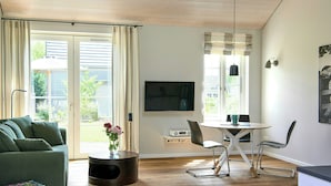 Un salon avec un canapé vert, une table basse, un téléviseur et un coin repas comprenant une table et des chaises.
