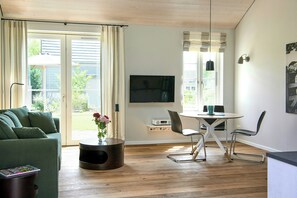 Ein Wohnzimmer mit einem grünen Sofa, einem Couchtisch, einem Fernseher und einem Essbereich mit Tisch und Stühlen.