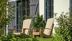 Deux chaises Adirondack en bois, placées dans un jardin, avec un bâtiment visible à l’arrière-plan.