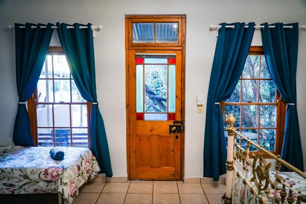 Une pièce avec une porte en bois, un lit recouvert d’une courtepointe à motifs floraux et un escalier agrémenté d’une rampe décorative.