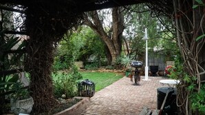 Une terrasse dallée avec une chaise blanche, une poubelle noire et un lampadaire blanc.