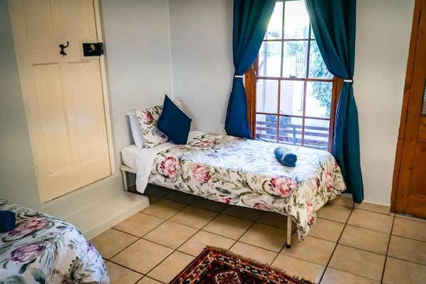 Ein Schlafzimmer mit Bett, einem Fenster mit Vorhängen, einer Tür und einem kleinen Tisch.