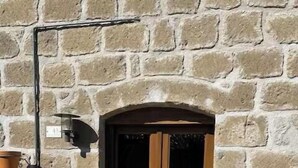 A stone wall with a wooden door, a metal rack, and a small step leading to the door. - Villa with heated pool in Toscana (San Quirico)