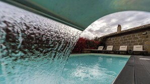 A swimming pool with a waterfall feature, lounge chairs, and a stone wall. - Villa with heated pool in Toscana (San Quirico)