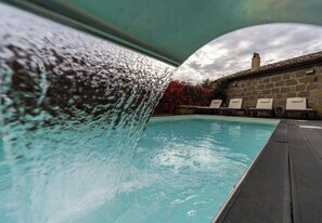 Ein Swimmingpool mit Wasserfall, Liegestühlen und einer Steinmauer.