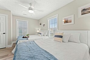 Ein Schlafzimmer mit zwei Betten, einem Deckenventilator und großen Fenstern mit Jalousien.