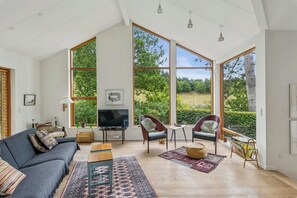 A spacious living room with a large TV, comfortable seating, and large windows offering a view of the outdoors. - Architect-designed house in Mols Bjerge (Ebeltoft)