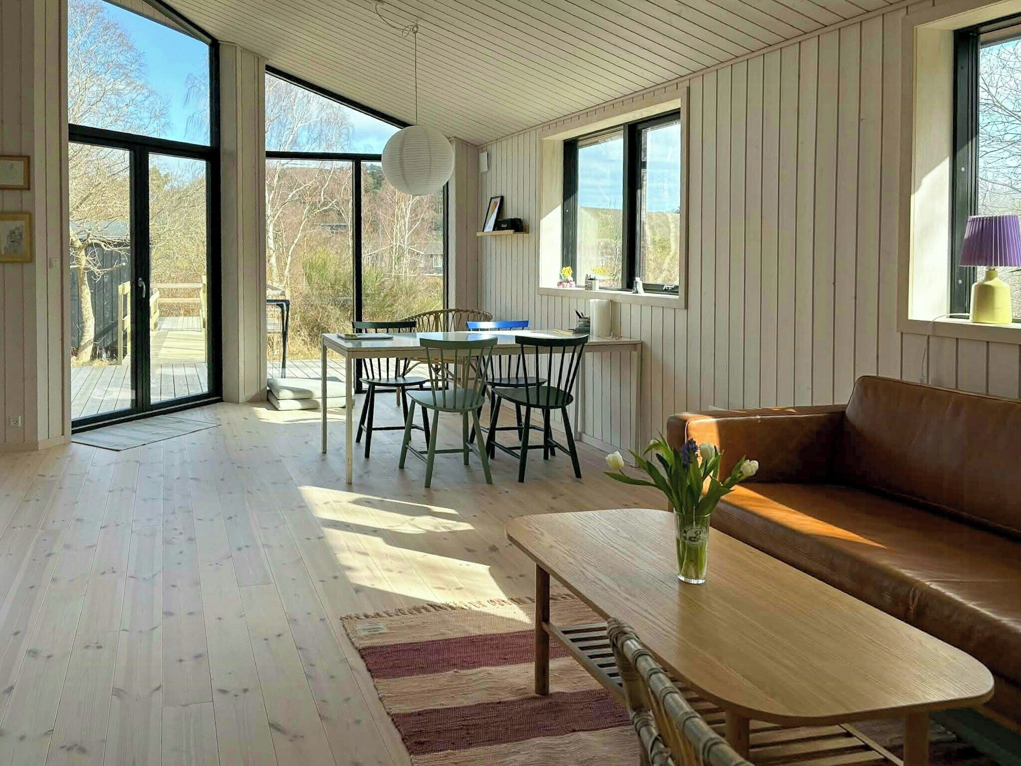 A spacious room with a wooden floor, a dining area with chairs and a table, a sofa, and large windows.