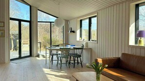 A spacious room with a wooden floor, a dining area with chairs and a table, a sofa, and large windows.