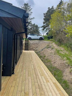 Een houten terras dat leidt naar een gebouw, met een auto op de achtergrond.