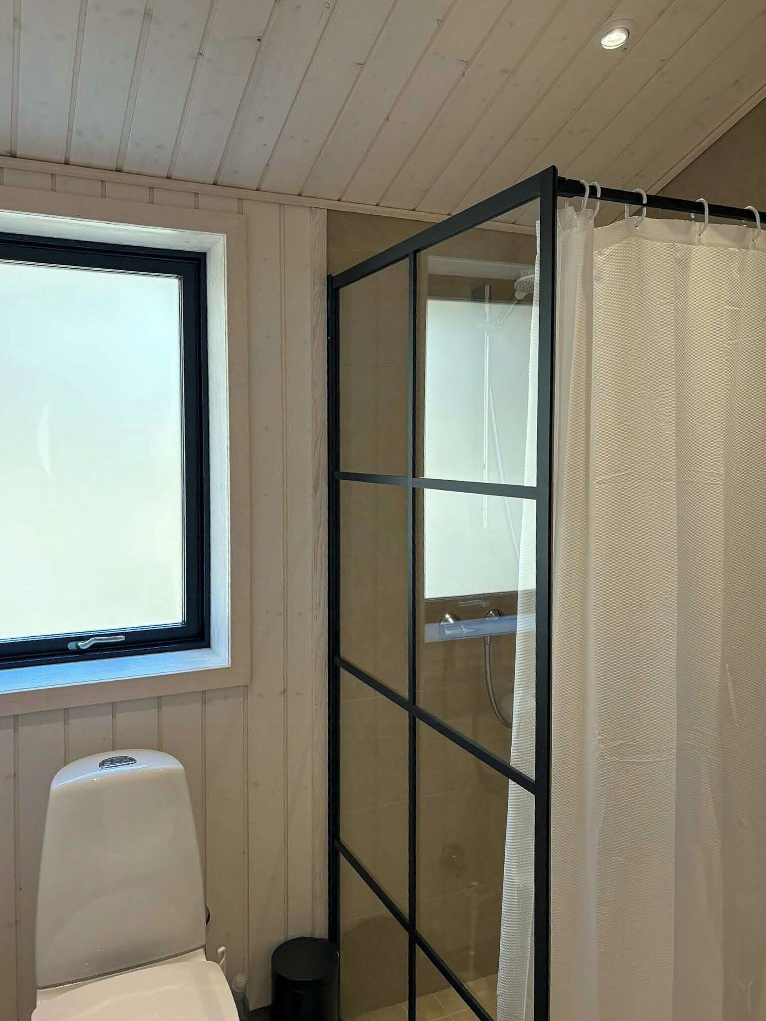 A bathroom with a window, a shower with a glass partition, and a toilet.