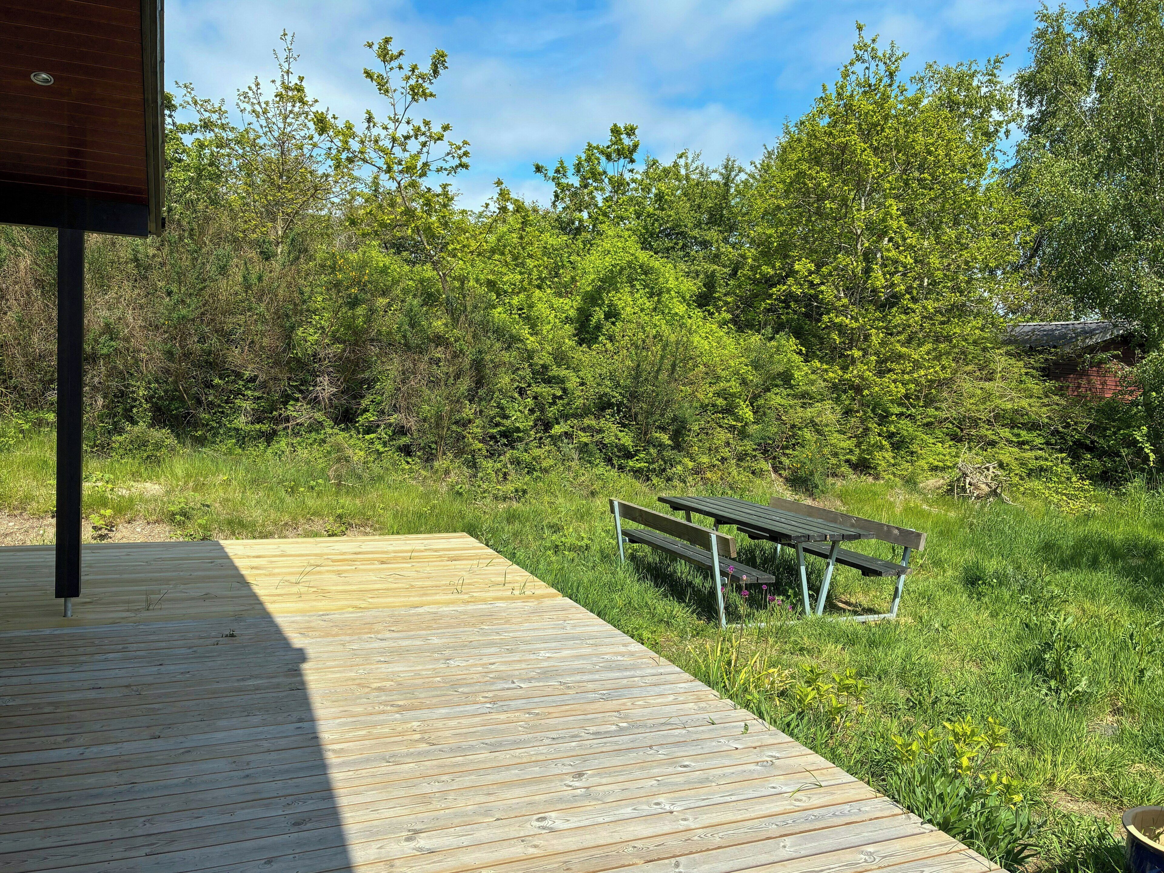 A wooden deck with a bench, surrounded by lush greenery and trees.
