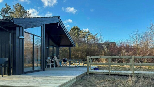 A modern cabin with a wooden deck, a covered outdoor seating area, and a view of the surrounding landscape.