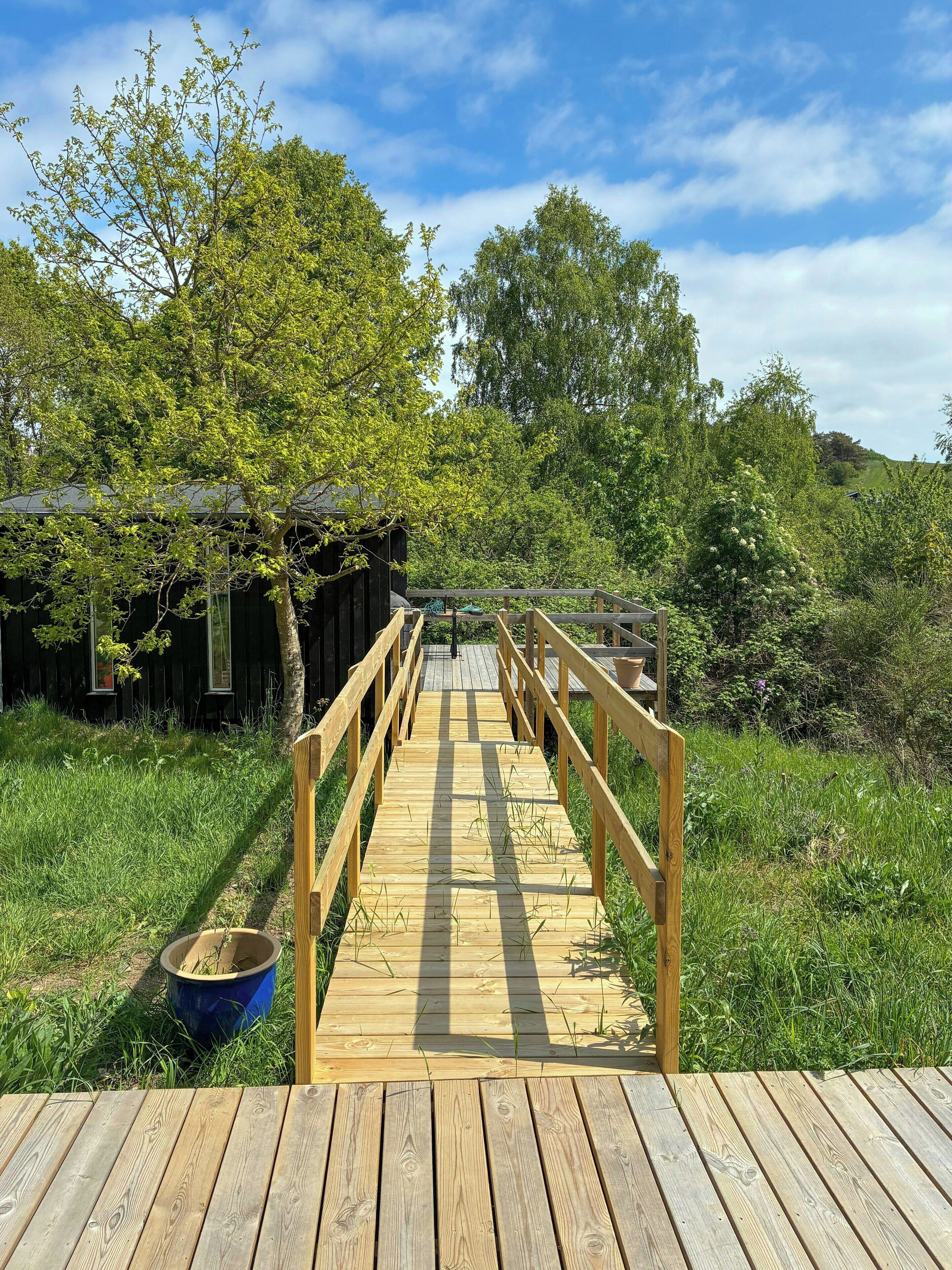 Eine Holzterrasse führt zu einem rustikalen Gebäude, umgeben von üppigem Grün.