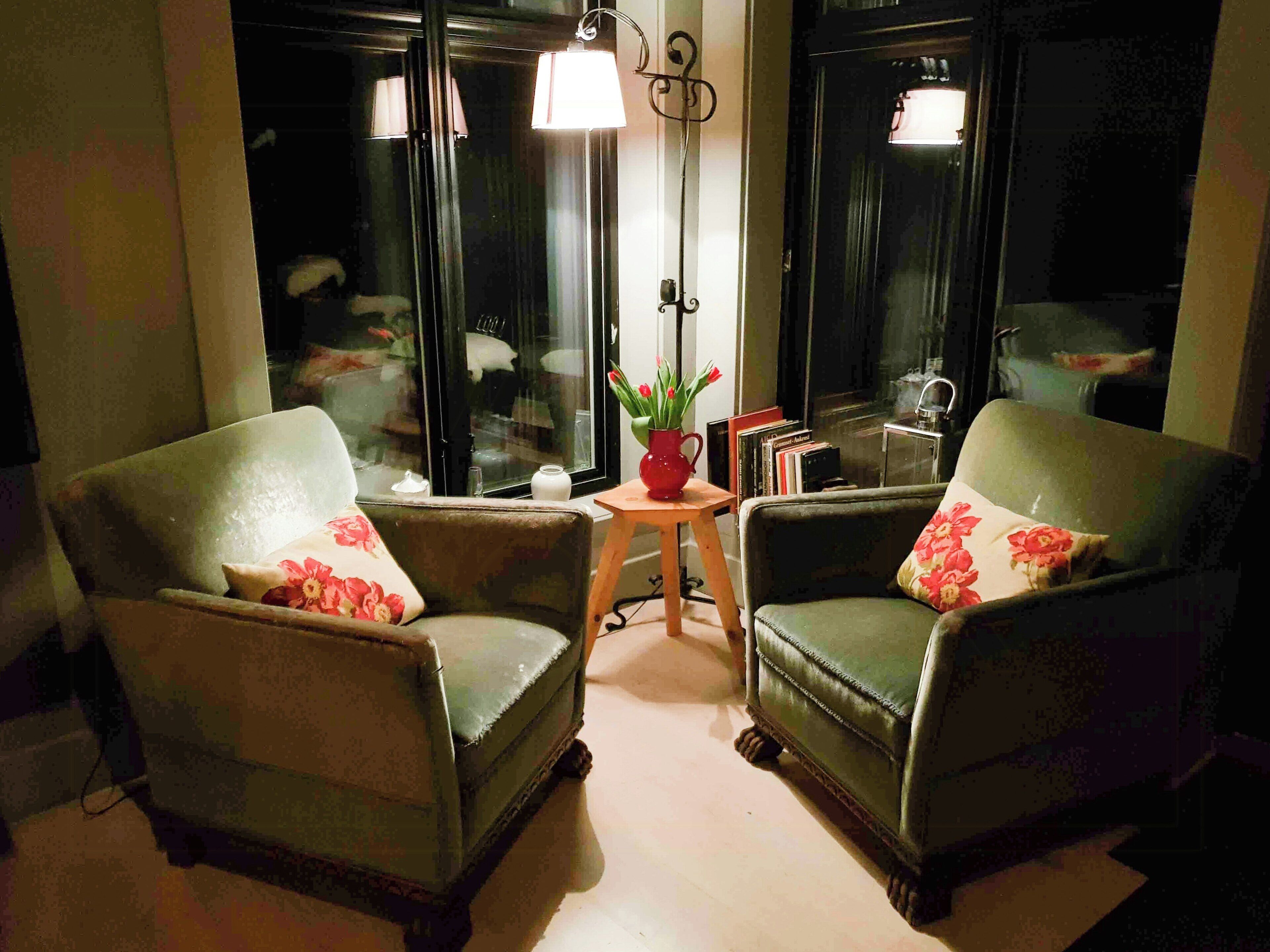 Two armchairs with floral cushions, a small table with a vase of flowers, and a floor lamp.