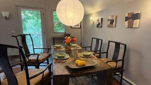 A dining room with a wooden table, chairs, a hanging light fixture, and artwork on the walls. - The Artist's Loft | Pet Friendly | Close to Torch (Alden)