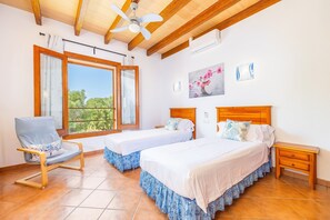 Ein Schlafzimmer mit zwei Betten, einem Sessel, einem Nachttisch und einem Deckenventilator.