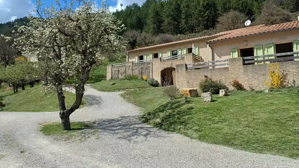 A rural house with a gravel path leading to it, surrounded by greenery and trees.
