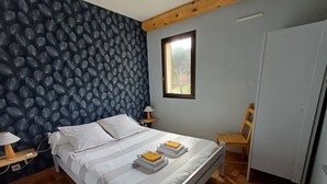 A bedroom with a bed, a nightstand, a lamp, a wooden chair, a wardrobe, and a window.