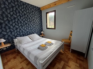Ein Schlafzimmer mit einem Bett, einem Nachttisch, einer Lampe, einem Holzstuhl, einem Kleiderschrank und einem Fenster.
