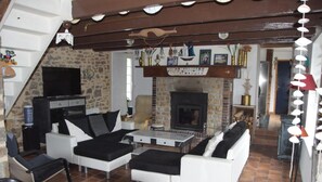 A cozy living room with a fireplace, black and white furniture, and a television. - Holiday Home “Fermette 5 Adults in the Countryside” with Private Terrace, Garden & Wi-Fi (Hudimesnil)