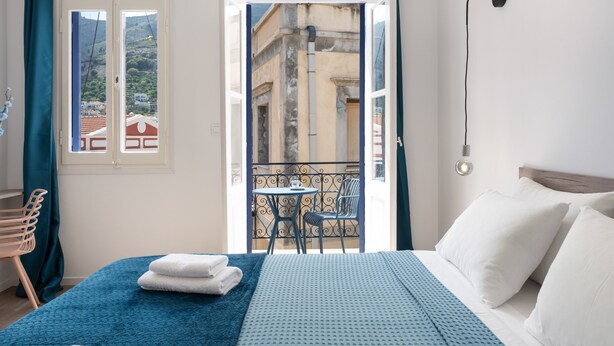 Quarto de hotel com cama, varanda com mesa e cadeiras e vista para edifícios.