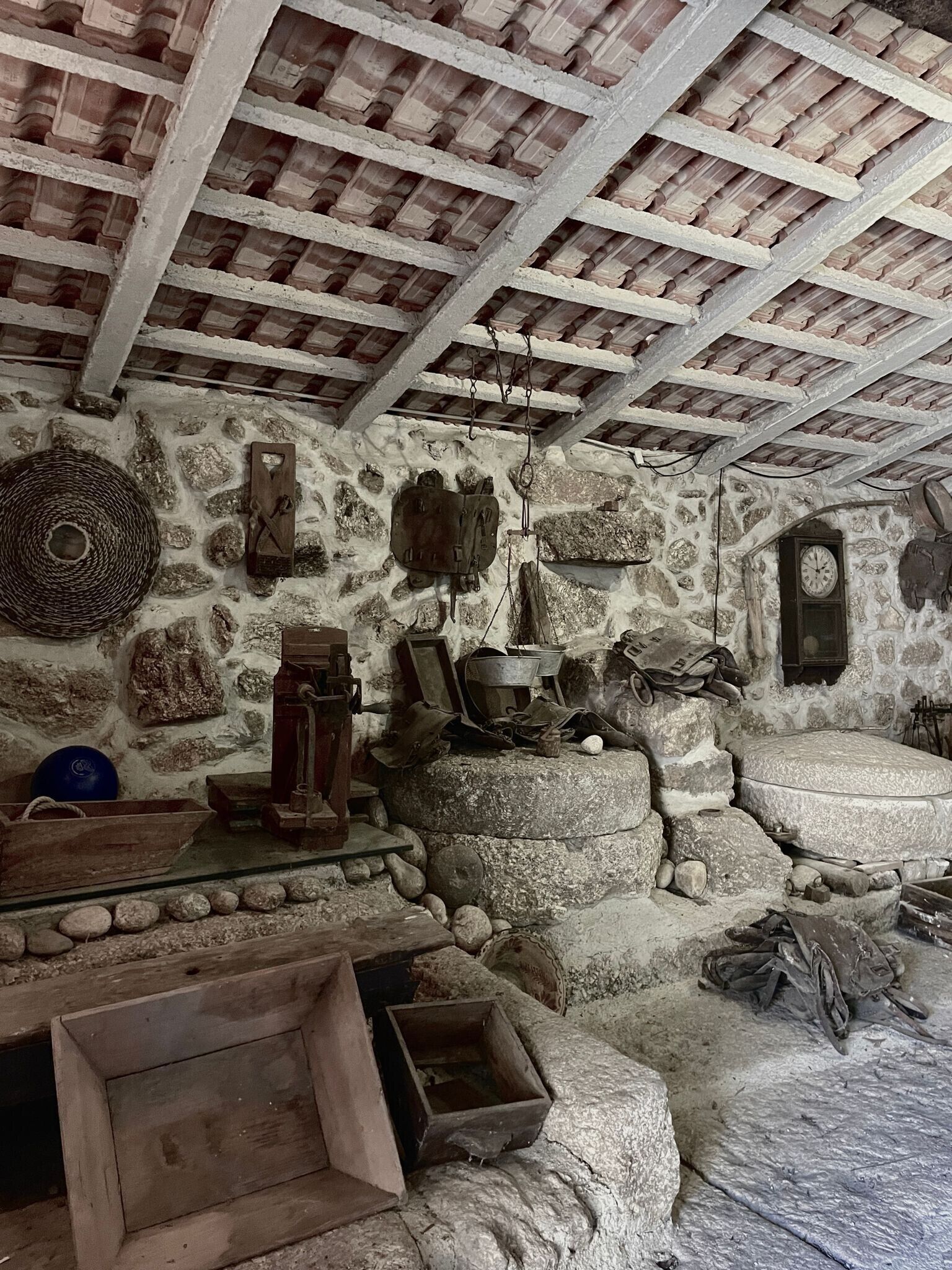 Interior rústico de pedra com teto de madeira, paredes de pedra e diversos utensílios e objetos.