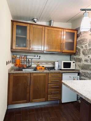 Eine Küche mit Holzausstattung, einer Mikrowelle, einem kleinen Kühlschrank und einer Steinwand.