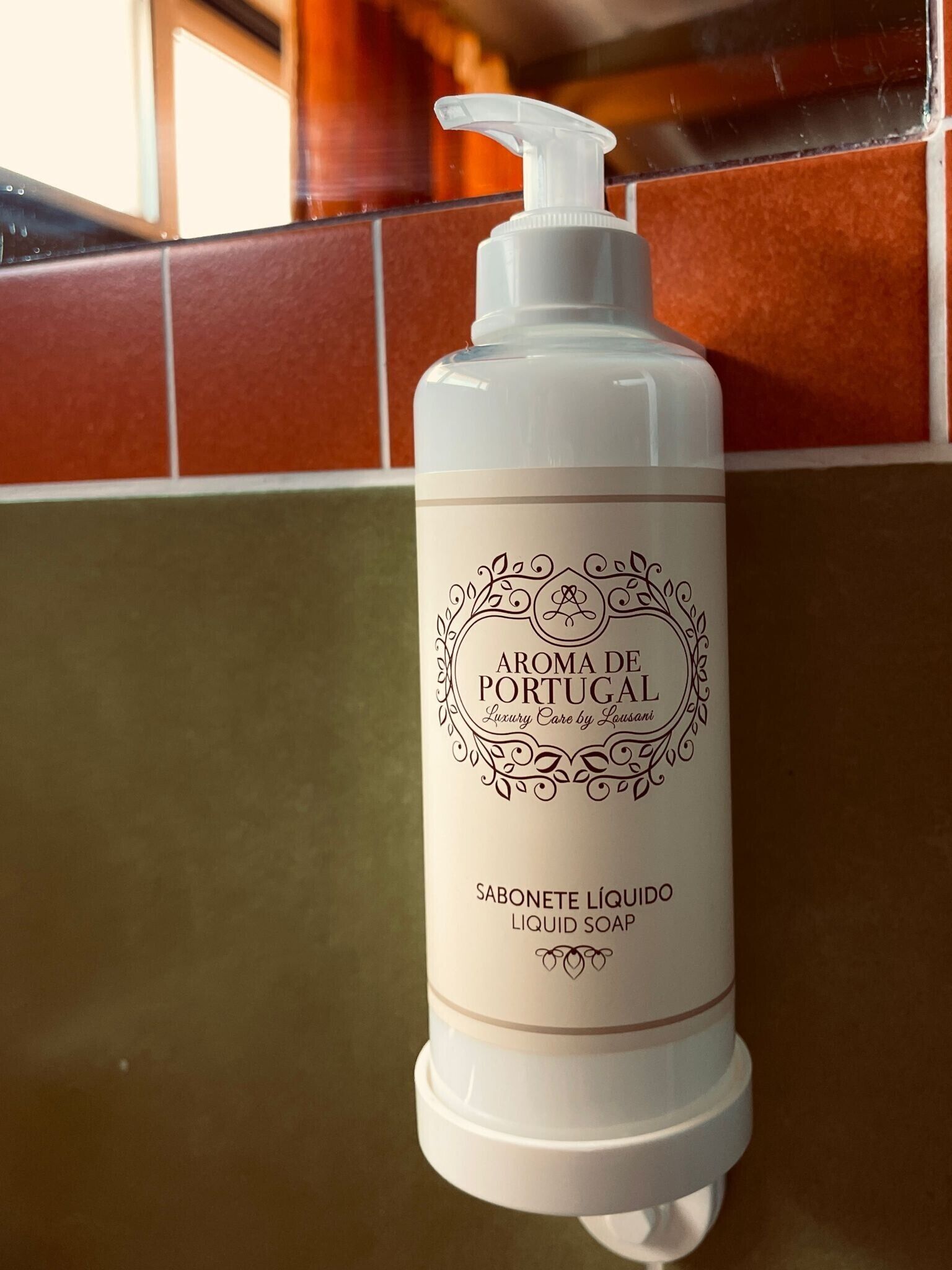 Una botella de jabón líquido blanco con dosificador de bomba, etiquetada como 'Aroma de Portugal,' sobre una superficie con baldosas.