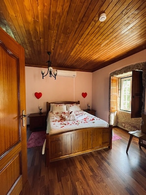 A wooden-framed bed with rose petals, a chandelier, and heart-shaped decorations on the walls. - Casa do Rio - Quinta do Moinho Apartment with Mountain View, Wi-Fi and Air Conditioning (Faia)