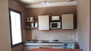 Een kleine keuken met een eettafel, stoelen, een magnetron en een plafondventilator.