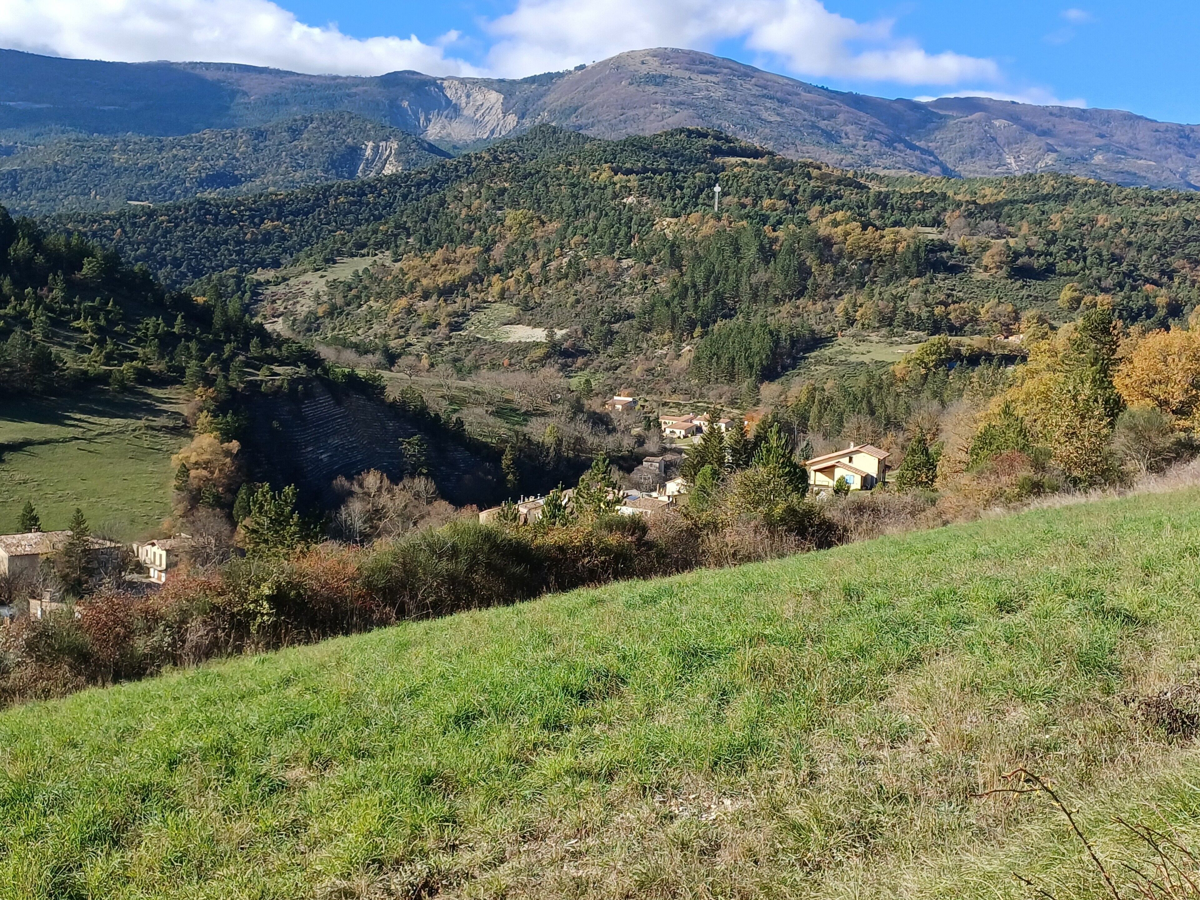 Un paisaje montañoso con un valle, casas dispersas y un cielo despejado.