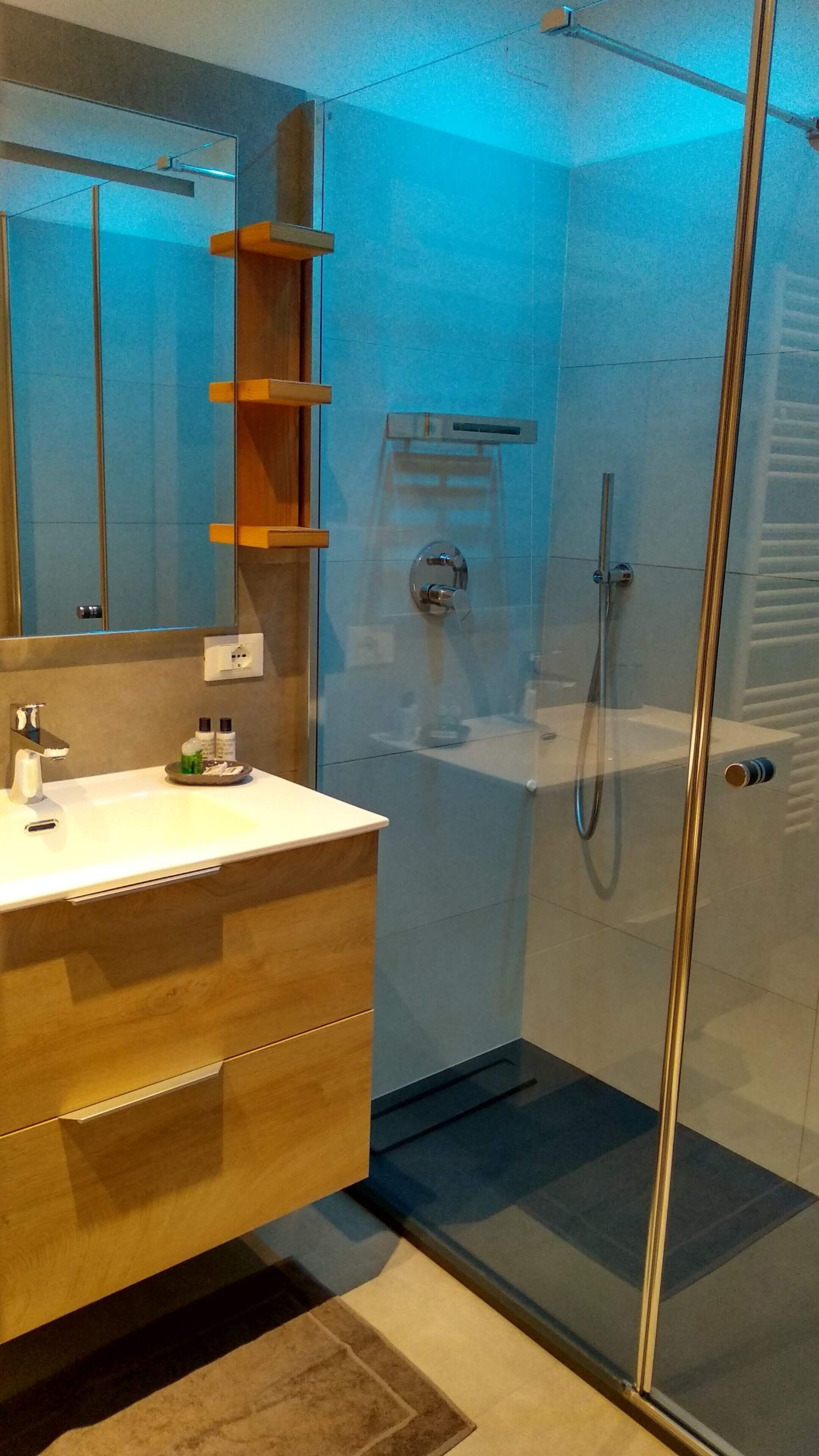 A modern bathroom with a glass shower enclosure, a wooden vanity, and a mirror above the sink.