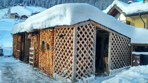 Una baita di legno coperta di neve, con facciata a reticello, una porta e una finestra.
