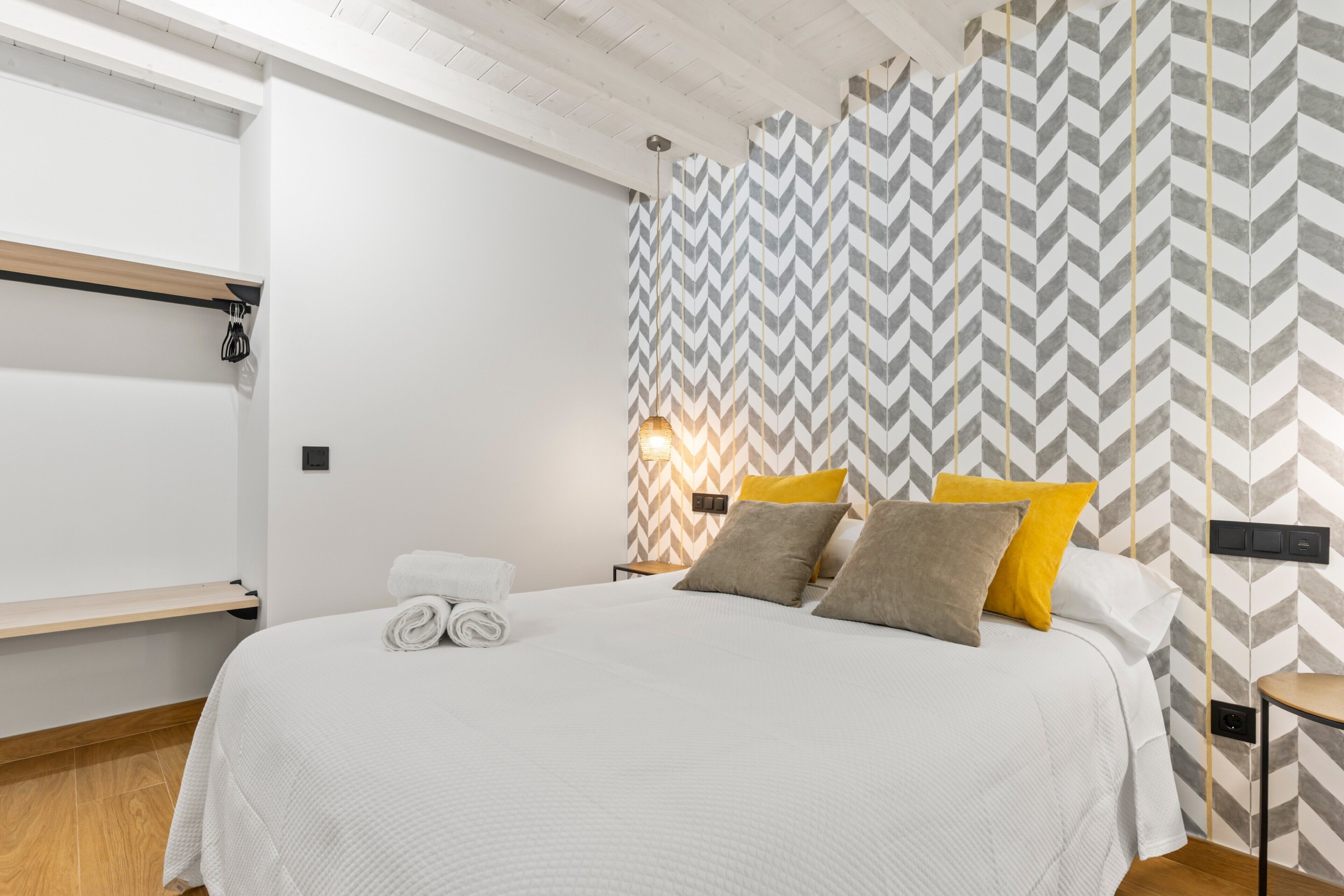 A modern hotel room with a large bed, a wooden floor, a white wall, and a chevron-patterned wall.
