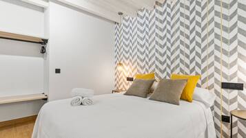 A modern hotel room with a large bed, a wooden floor, a white wall, and a chevron-patterned wall.