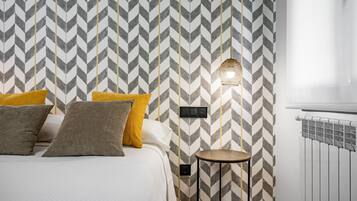 Een slaapkamer met een zigzaggemêleerde wand, een bed met veel kussens, een klein rond tafeltje en een wandlamp.