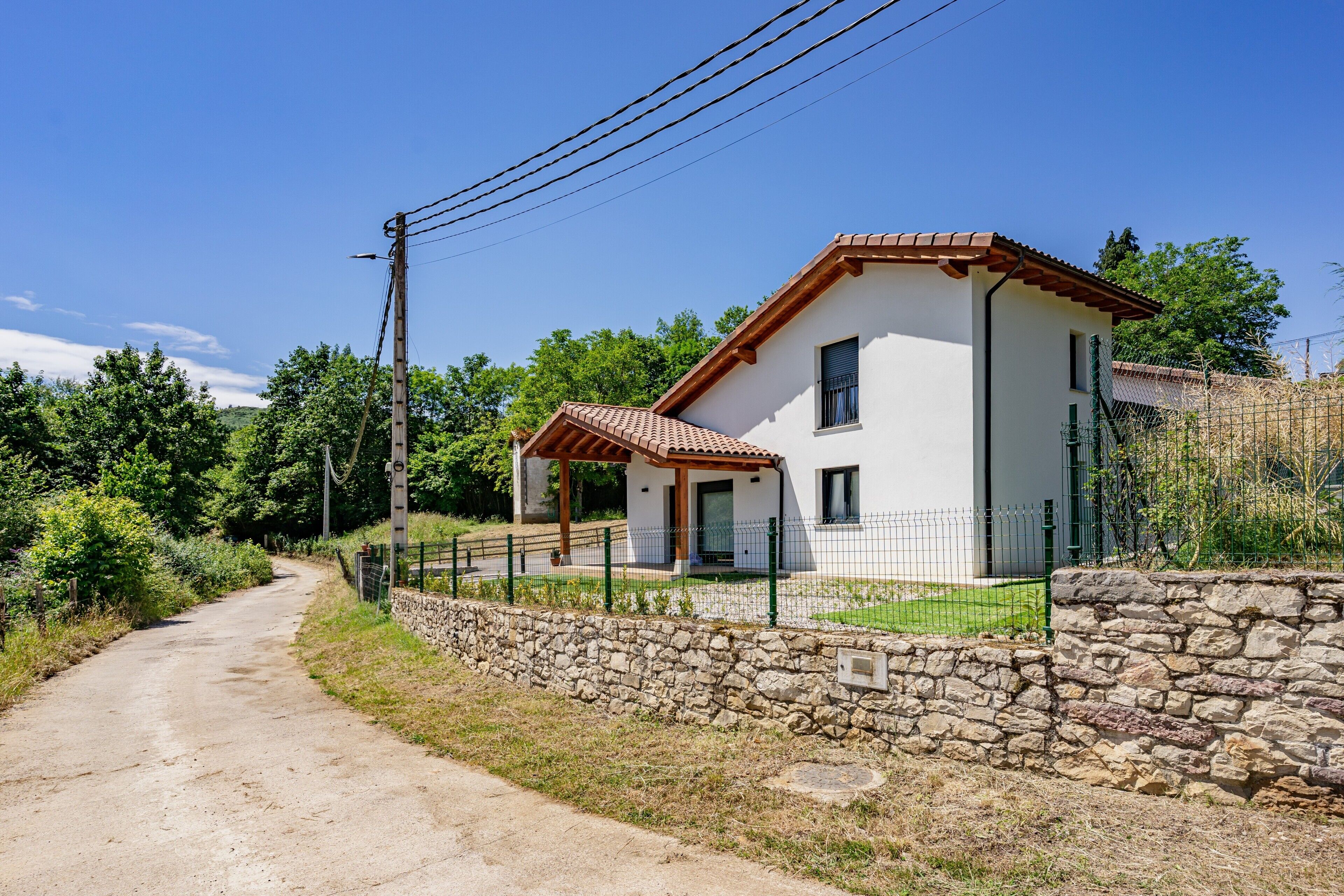 A two-story house with a stone wall and a paved driveway.
