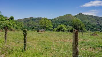 Un paysage rural avec une structure en bois, un champ clôturé et des collines en arrière-plan.