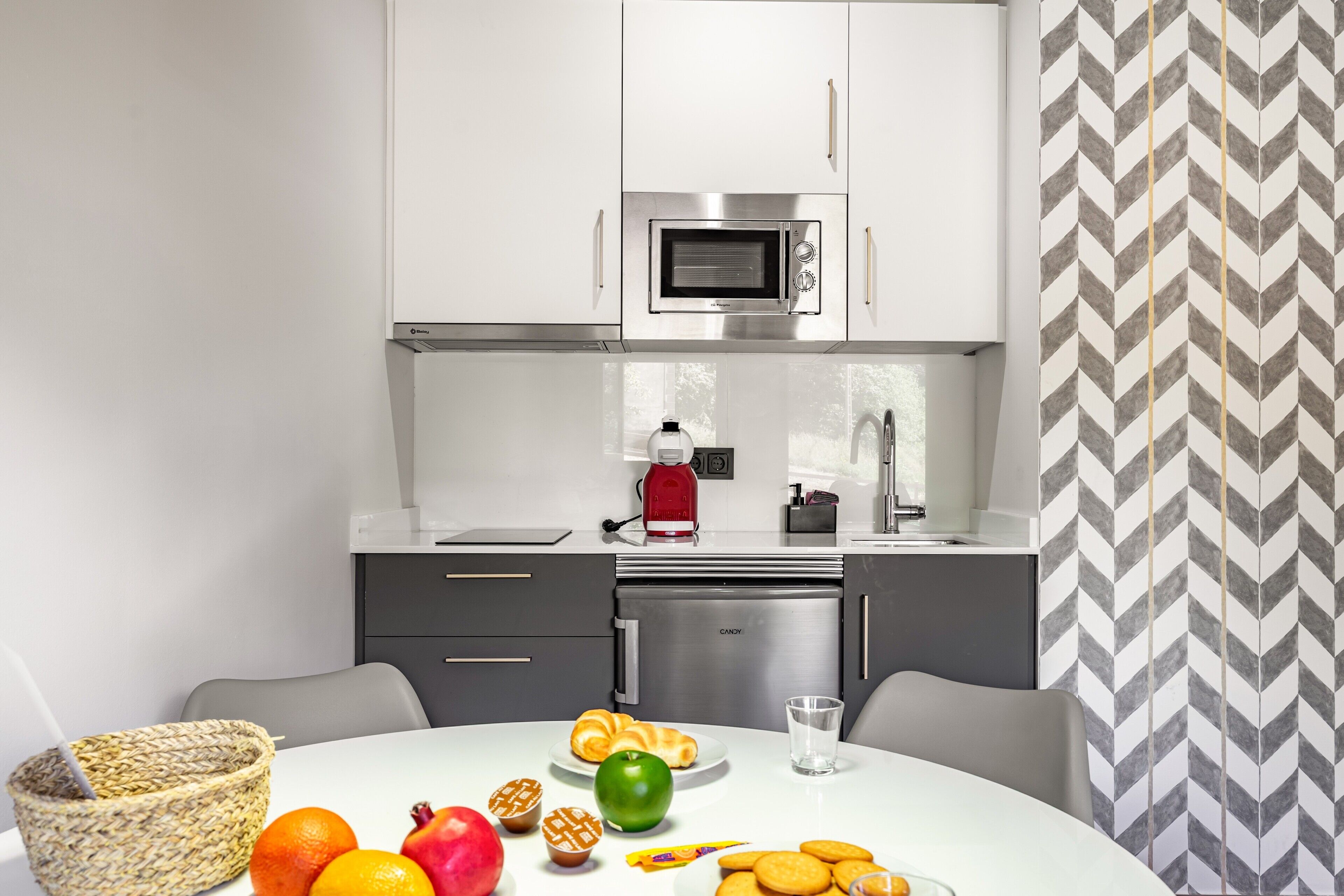Una cucina moderna con mobili bianchi, un forno a microonde, una macchina per caffè e un frigorifero.