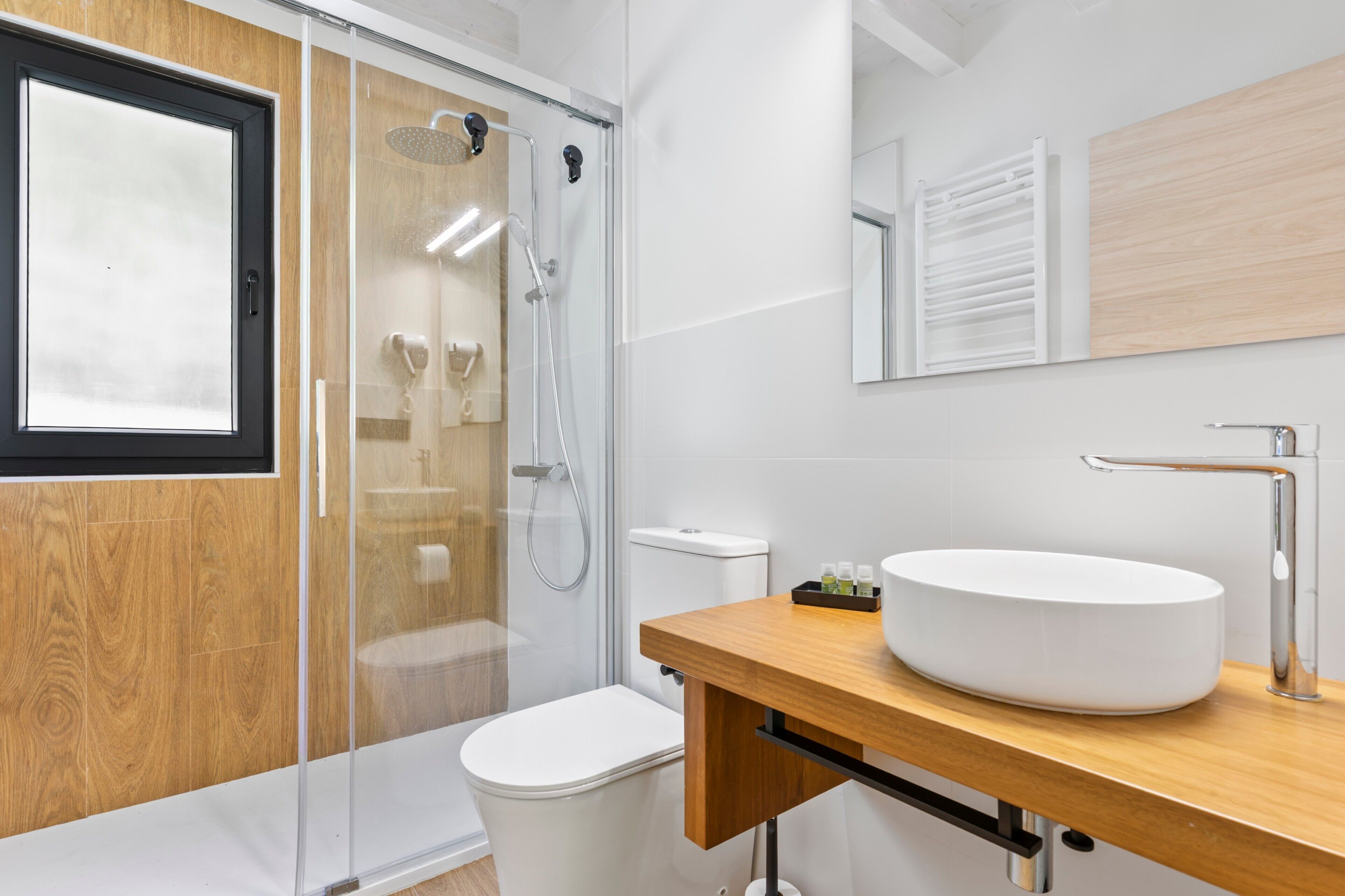 A modern bathroom with a glass shower enclosure, a white toilet, a wooden vanity with a white sink, and a mirror above the sink.